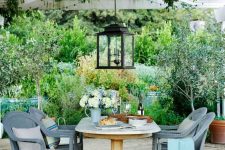 a small Mediterranean outdoor dining space with a wooden table, slate grey wicker chairs, blooms and greenery and a large pendant lantern