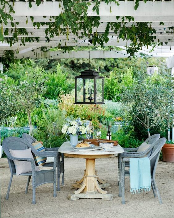 a small Mediterranean outdoor dining space with a wooden table, slate grey wicker chairs, blooms and greenery and a large pendant lantern