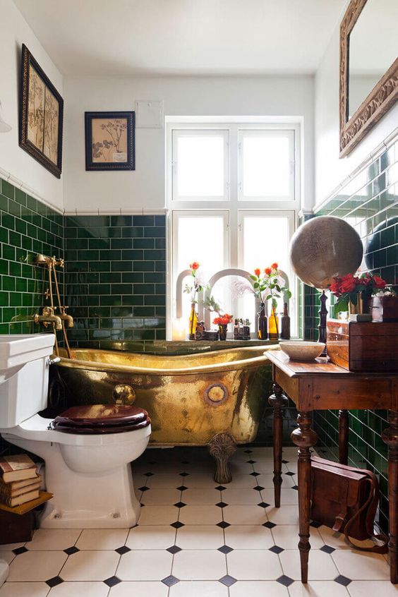 a small vintage bathroom with green subway tiles, a vintage stained vanity, artwork and a mirror, blooms and some decor