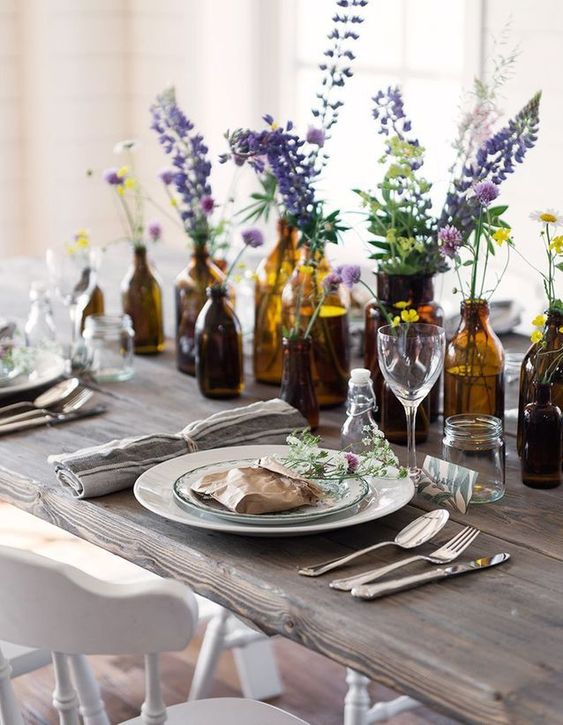a summer table lined up with apothecary bottles and jars with bright blooms in them for a beautiful look