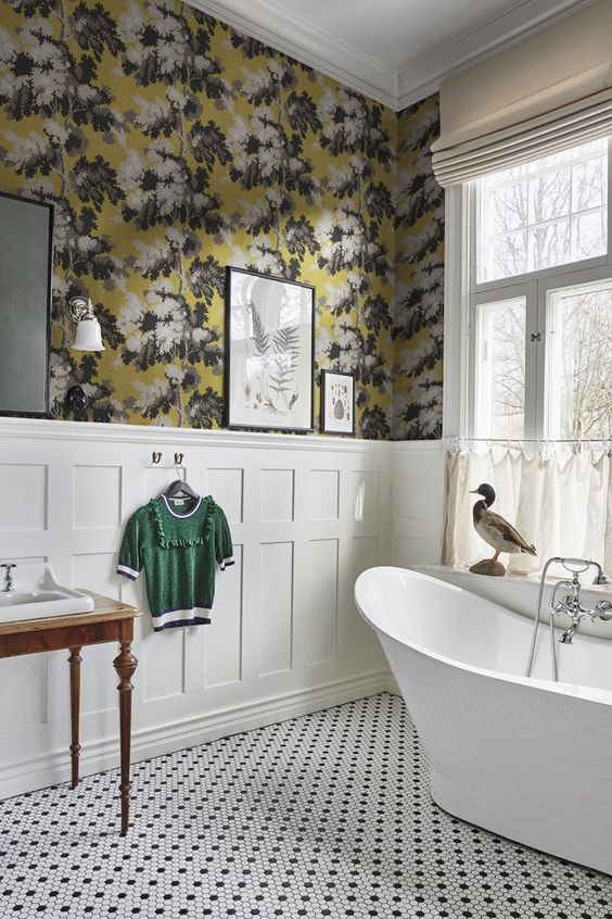 a vintage bathroom with moody floral wallpaper, creamy paneling, a free-standing bathtub, black and white tile floor and a vintage vanity