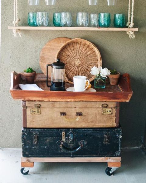 a vintage storage unit on casters composed of two vintage suitcases and a large tray, with baskets and some blooms