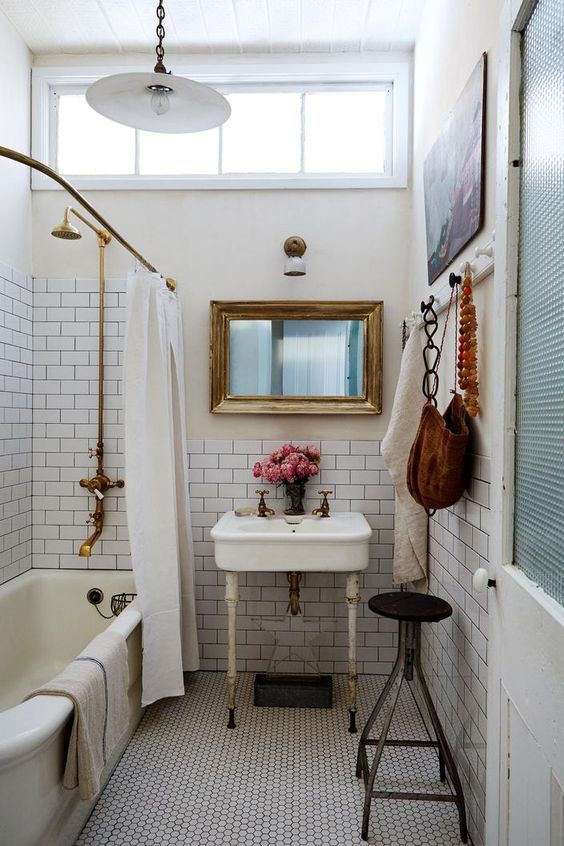 a white vintage bathroom with white subway and penny tiles, a bathtub, artwork, a black stool and a free-standing sink