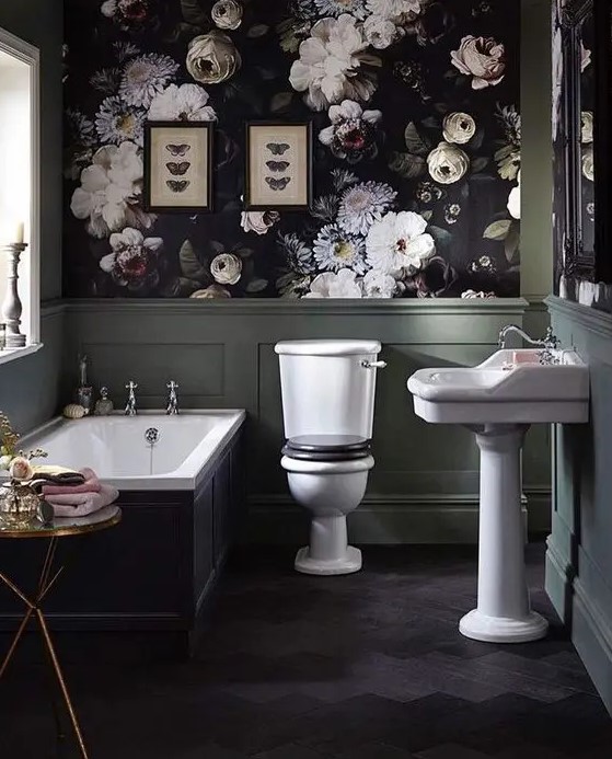 an exquisite Gothic bathroom with dark floral wallpaper and green panels, a tub with black panels, white appliances, a chic table and butterfly art