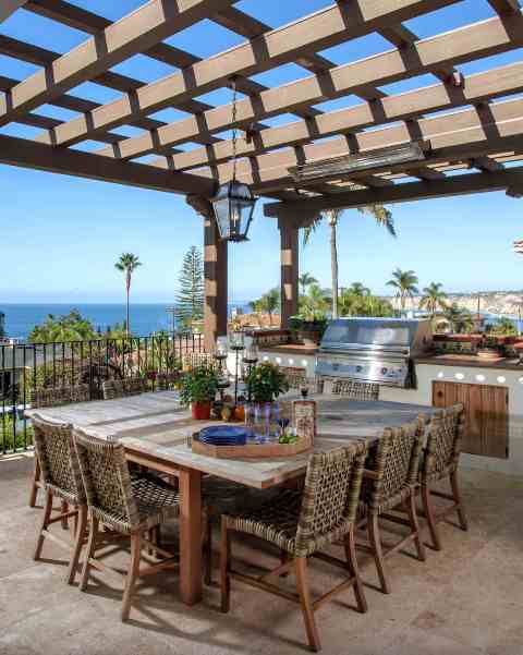 an outdoor Mediterranean dining space with a large table, wicker chairs, a pendant lamp and an outdoor kitchen plus a fantastic view