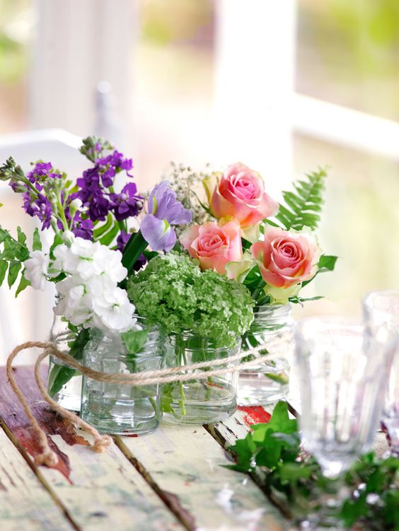 clear jars with various summer blooms and twine are a cool and simple summer decoration or centerpiece