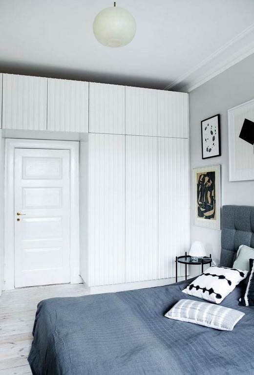 a Scandinavian bedroom with a grey upholstered bed with grey bedding, a gallery wall, a series of white wardrobes is a lovely space