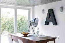 a Scandinavian dining space with a tin tile ceiling, a stained table and white chairs, a monogram and some lamps
