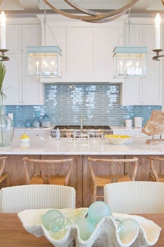 a beach cottage kitchen with white shaker cabinets, a glossy blue tile backsplash, blue and white pendant lamps and a wooden kitchen island