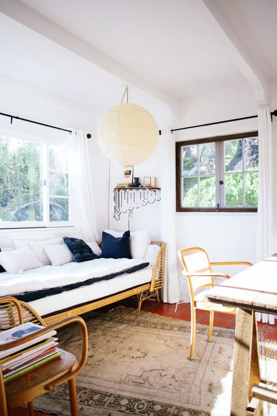 a beach home office with a wooden desk, rattan chairs and a daybed, a pendant lamp and navy and white pillows