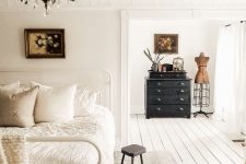 a beautiful Scandinavian bedroom with a chic vintage patterned ceiling, a white metal bed with neutral bedding, a black dresser and a lovely chandelier