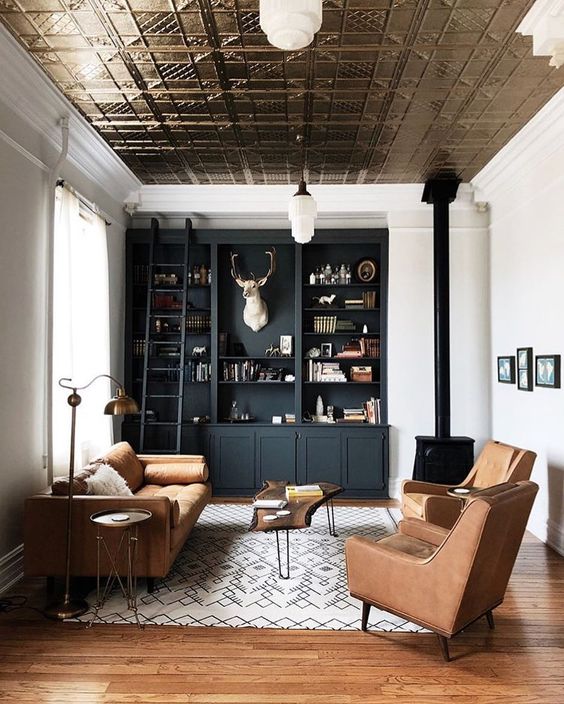a beautiful and welcoming lviing room with a tin tile ceiling, a black built in storage unit, a fireplace, amber leather seating furniture and a rug
