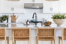 a beautiful beach kitchen in white, with shaker cabinets, a glossy white tile backsplash, a large kitchen island with woven stools and woven pendant lamps