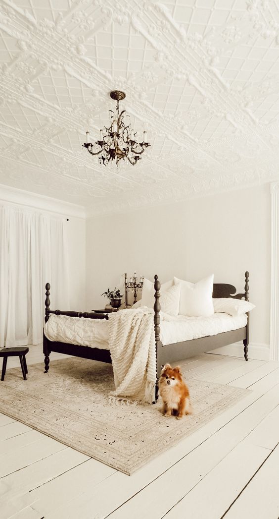a beautiful neutral bedroom with a patterned ceiling, a black carved wooden bed with white bedding, a crystal chandelier