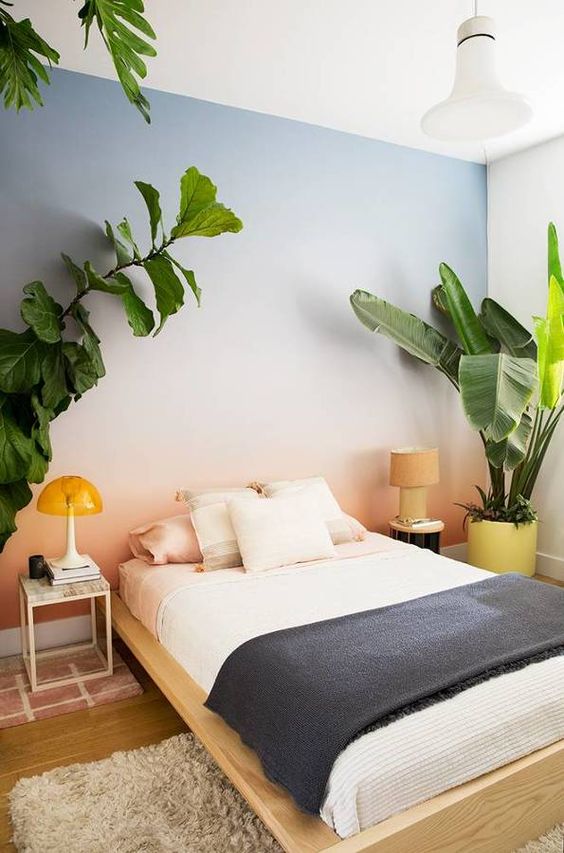 a bedroom with a gradient blue to coral accent wall, mismatching nightstands, potted plants and a pendant lamp