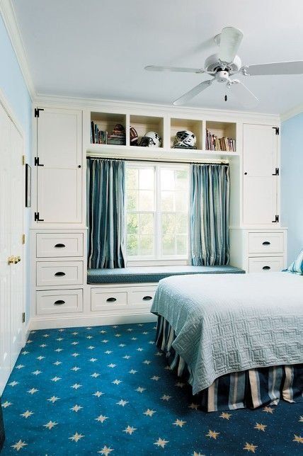 a blue and white bedroom with blue walls and a navy rug, a bed with blue bedding, a neutral storage unit with drawers and blue curtains and an upholstered bench