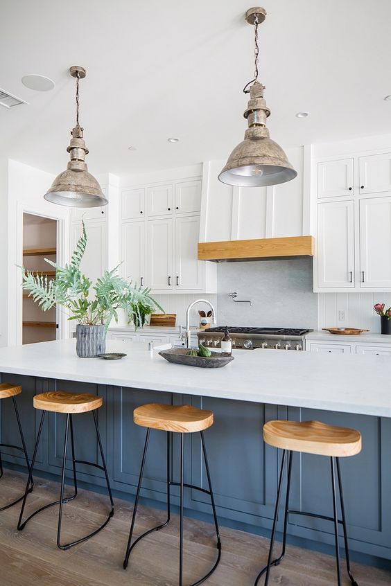 a bold and catchy beach kitchen with white shaker cabinets, a blue kitchen island, wooden stools and shabby metal pendant lamps