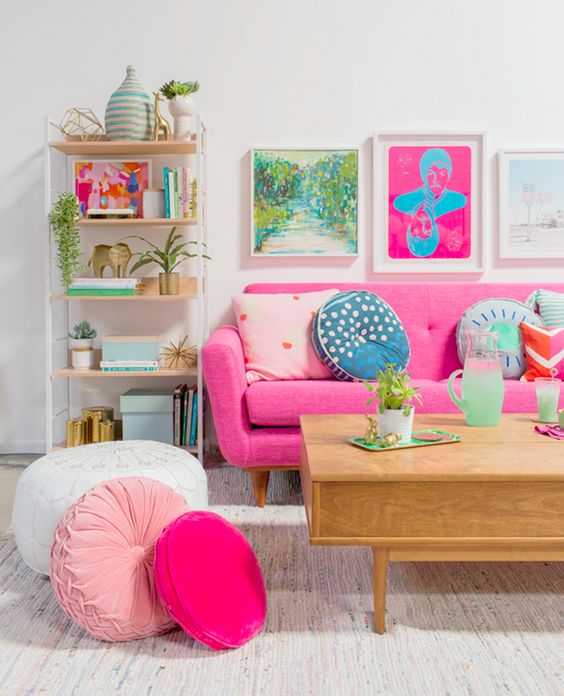a bold living room with colorful artworks, a pink sofa and pink and blush pillows plus printed ones