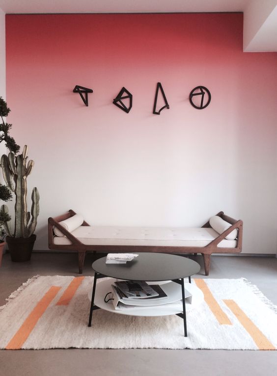 a bold space with an ombre red accent wall, a pretty daybed with neutral pillows, a tiered coffee table and potted plants
