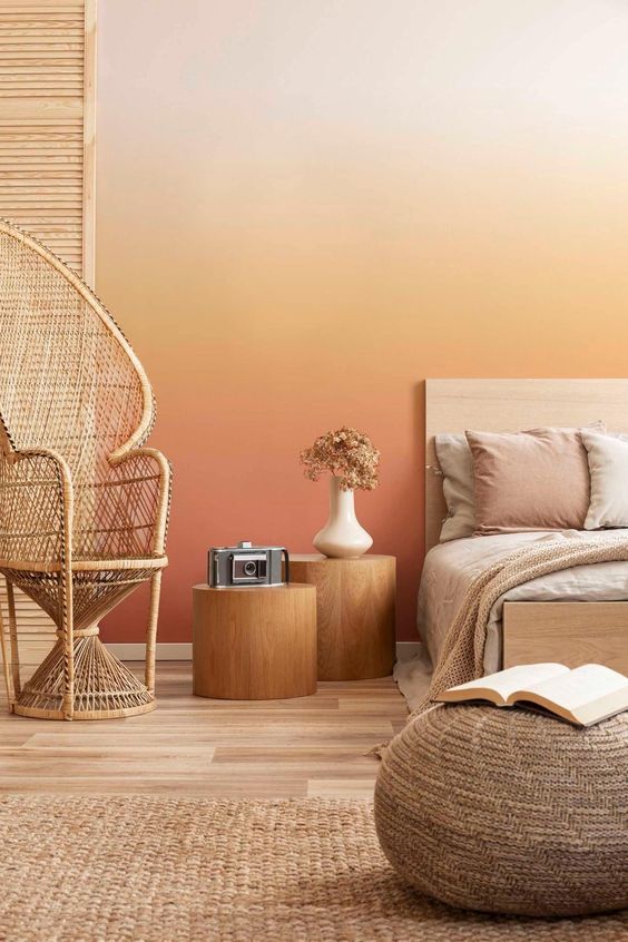 a bold warm-colored bedroom with a gradient wall from neutral to rust, a bed with neutral bedding, tree stump nightstands, a papasan chair
