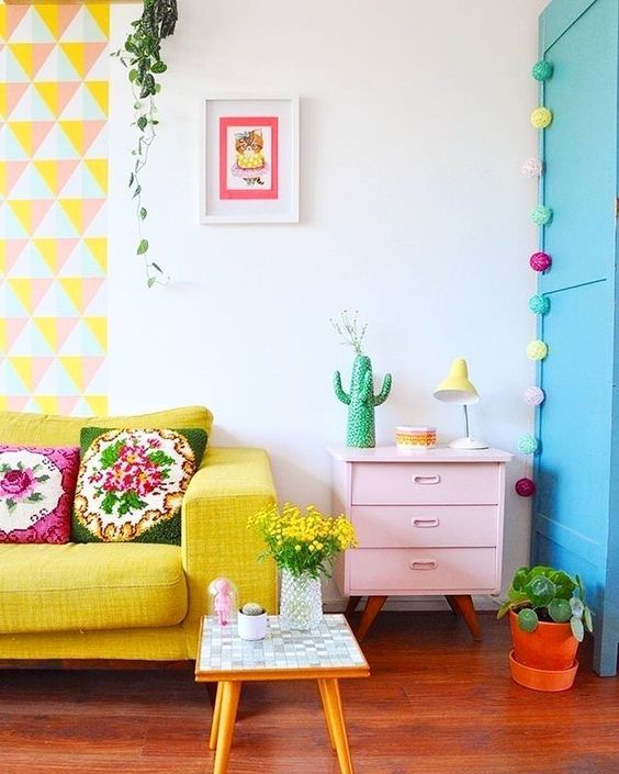 a bright geometric hanging, a yellow sofa, a pink dresser, colorful garlands and blooms and greenery in pots