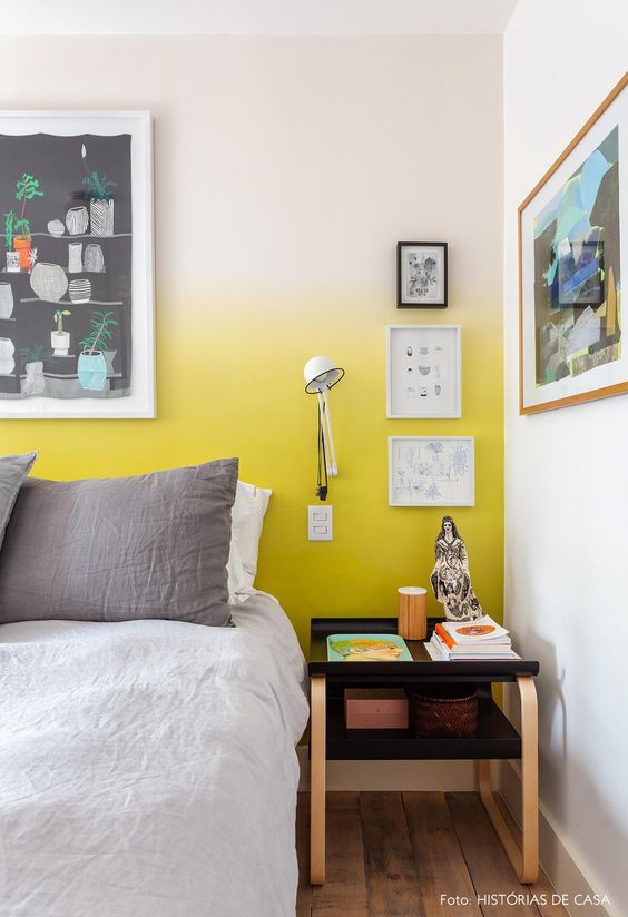 a catchy bedroom with a yellow ombre wall, a bed with neutral bedding, a black tiered nightstand, a gallery wall