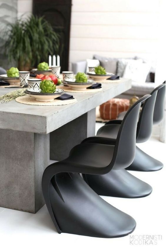 a catchy elcectic outdoor space with a concrete table, black curved chairs and a wicker sofa with neutral pillows