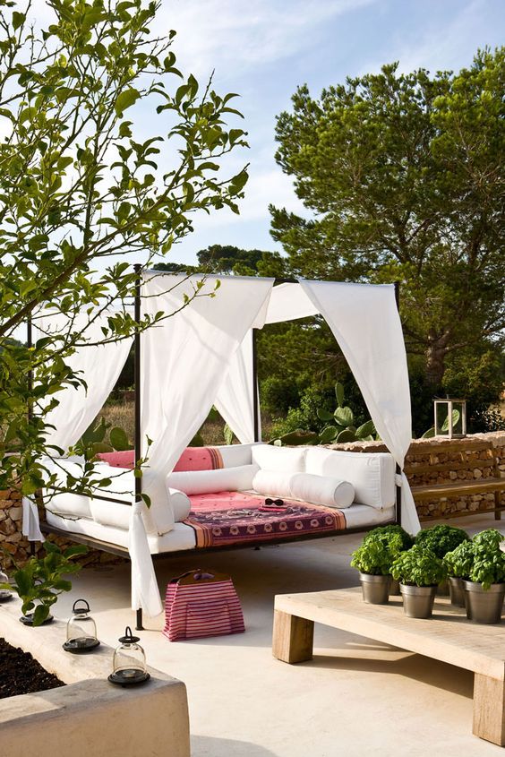a chic outdoor bedroom with a metal canopy bed, bright bedding, candle lanterns and potted greenery around