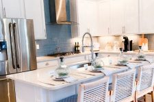 a coastal chic kitchen with white shaker cabinets, a blue tile backsplash, a large kitchen island with blue woven sotols and built-in lights