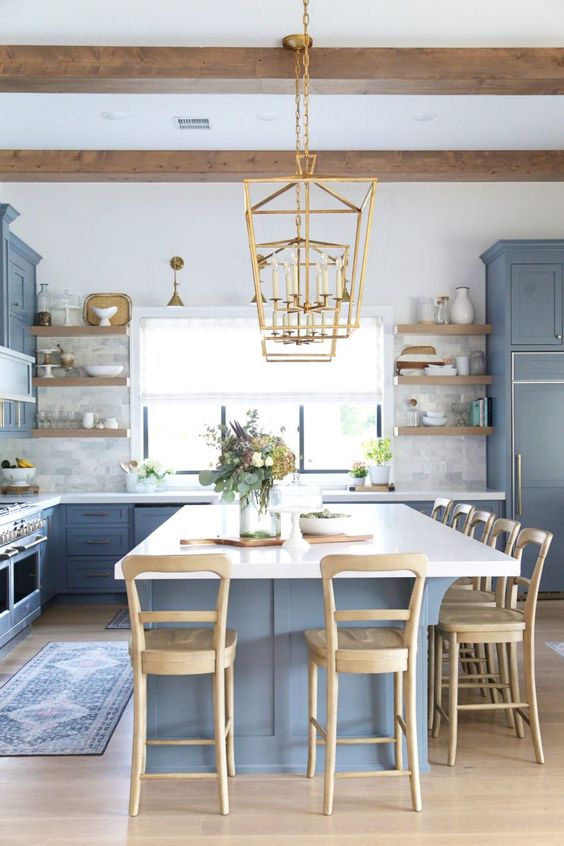 a coastal farmhouse kitchen with classic blue cabinetry and a kitchen island, wooden stools, beams and shelving and touches of gold