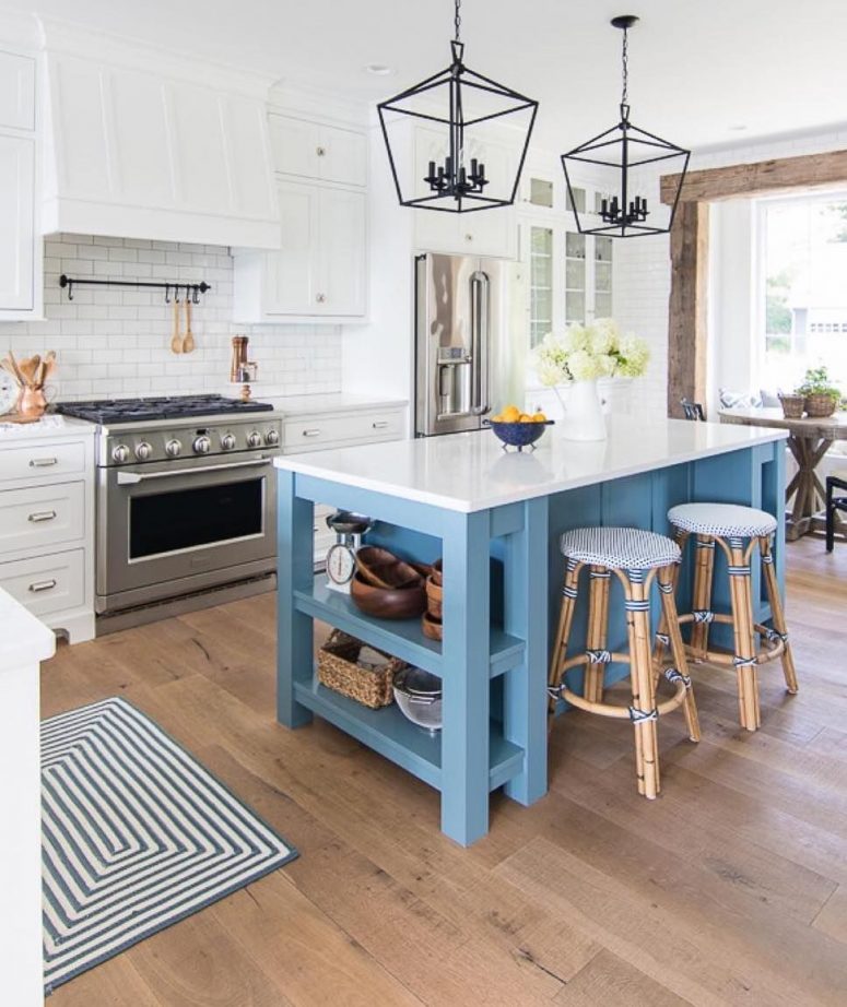 a coastal kitchen with white cabinets, a white tile backsplash, a blue kitchen island, rattan stools, blakc metal lamps