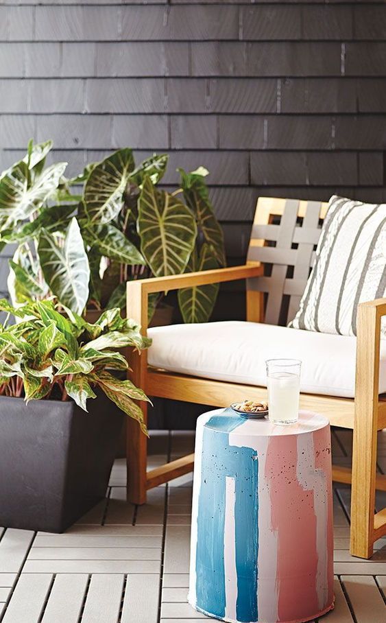 a cozy outdoor sitting nook with a neutral chair, potted plants, a cocnrete stool painted bright colors is lovely
