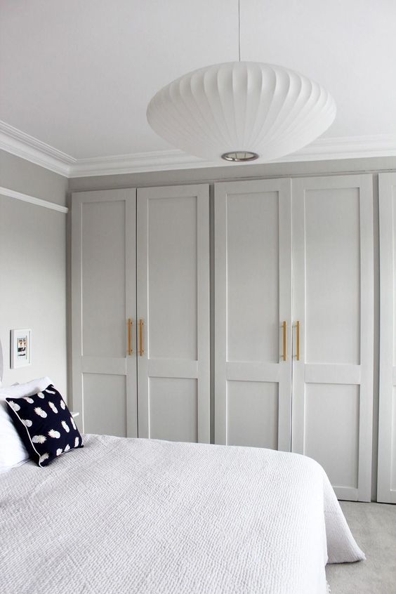 a dove grey bedroom with wall to wall wardrobes, a bed with neutral bedding, a paper pendant lamp and gold touches is a lovely idea