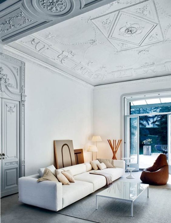 a fantastic neutral lving room with a gorgeous stucco ceiling and doors, a modern white sofa, a low coffee table and a leather chair