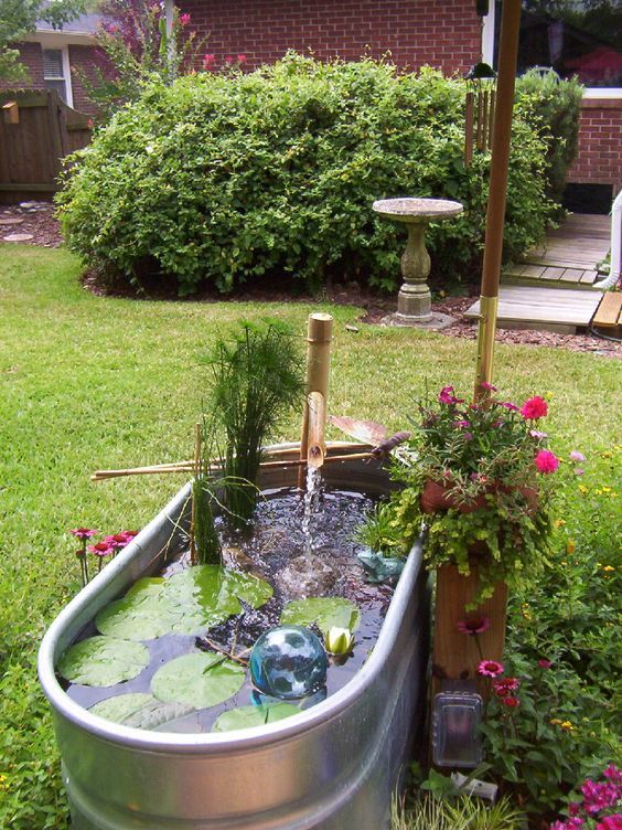 a galvanized stock tank water garden with a bamboo pump head and fish, water lilies and a blue glass ball