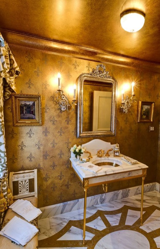 a gorgeous and refined powder room with a gold ceiling and gold furniture legs and faucets
