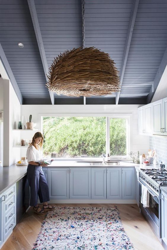 a lovely beach kitchen with light blue cabinets, a window instead of a backsplash, a unique woven pendant lamp