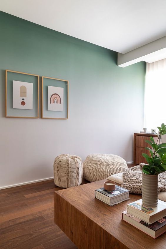 a lovely boho living room with an ombre green accent wall, a mini gallery wall, a stained dresser, a couple of neutral poufs and a stained table with books and plants