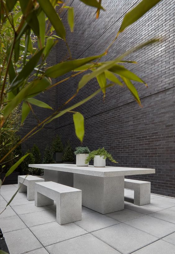 a minimalist outdoor dining space with a large concrete table and benches and potted greenery is a sleek and edgy nook