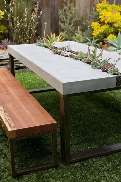 a modern outdoor dining space with a concrete and metal table, wood and metal benches and succulents growing in the table