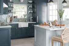 a moody coastal kitchen with navy cabinetry, a slate grey tile backsplash, a light blue kitchen island plus vintage pendant lamps