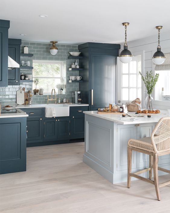 a moody coastal kitchen with navy cabinetry, a slate grey tile backsplash, a light blue kitchen island plus vintage pendant lamps