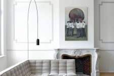a neutral French living room with a stucco ceiling and paneled walls, a vintage fireplace, a grey modern sofa and a pouf and a floor lamp