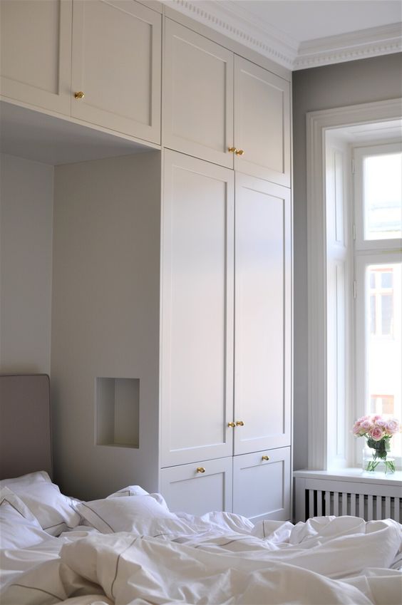a neutral Scandinavian bedroom with neutral built-in wardrobes that give a lot of storage space and a built-in bed