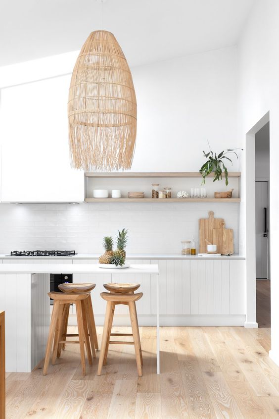 a neutral beach kitchen with white beadboard cabinets, a white tile backsplash, a kitchen island with a sitting space and a statement pendant lamp