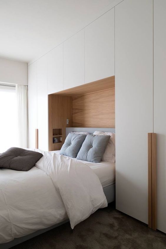 a neutral bedroom with a large sleek storage unit, a niche with built in shelves and a bed with cozy and soft bedding is amazing