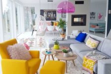 a neutral living room with a bright yellow chair, boho textiles, a pink pendant lamp and potted plants