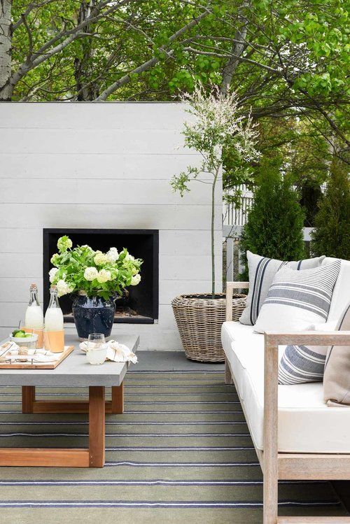 a neutral modern outdoor living room with a fireplace, a concrete coffee table, a light-stained sofa with neutral upholstery