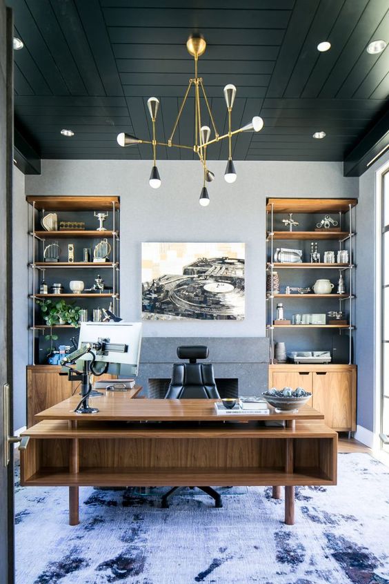 a refined beach home office with grey walls, a black wooden ceiling, built-in storage units and a large stained desk plus a sea-inspired rug