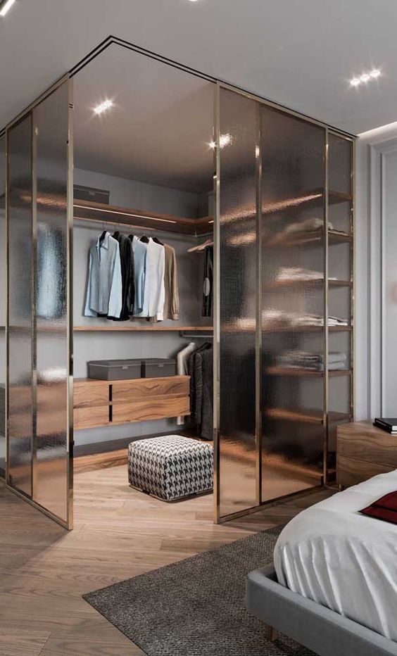 a refined bedroom with neutral paneled walls, a grey bed, a walk-in closet and glass sliding doors, lights and open shelves